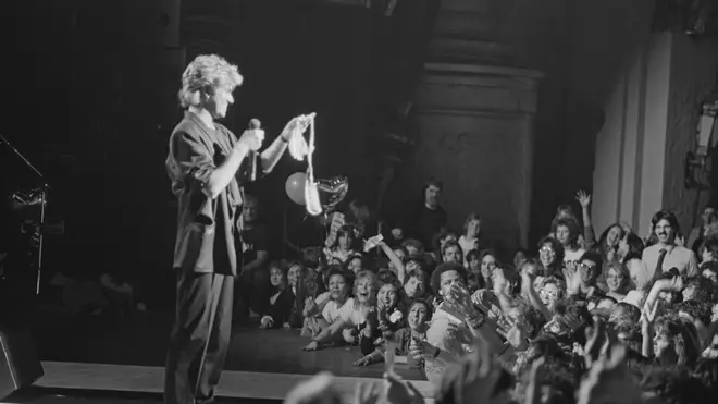 George Michael holds up a bra thrown onstage during a concert at the Beacon Theatre in New York during the North American leg of their 1985 world tour on 14th February 1985.