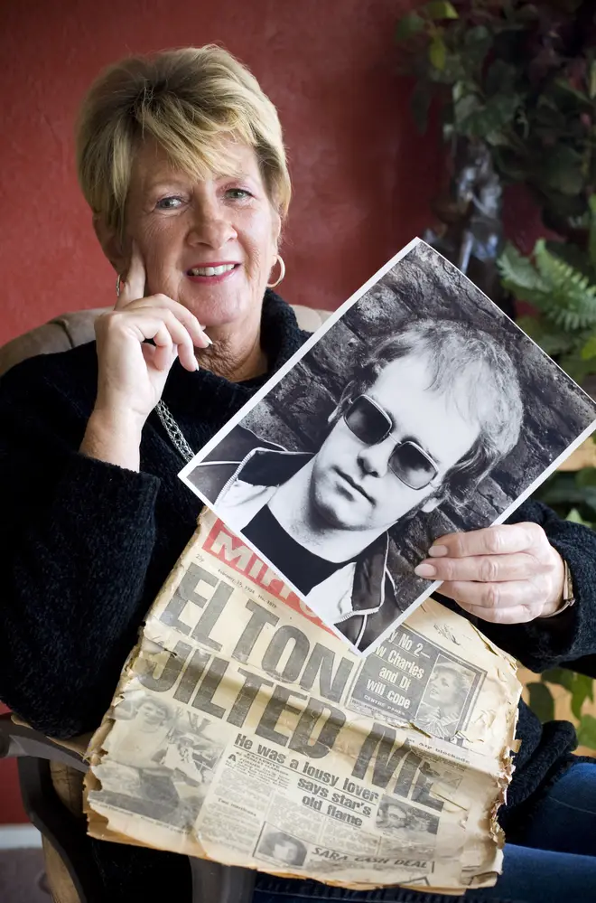 Elton John's ex-fiancé Linda Hannon holding a newspaper and photo of the singer in 2010