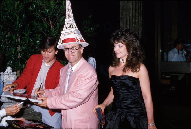 Sir Elton John wears an Eiffel Tower hat as he signs an autograph while his now ex-wife Renate Blauel looks on