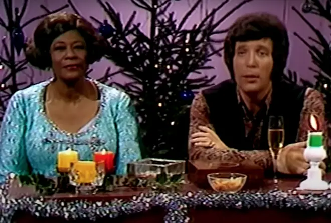 The pair are seen on the video sitting in front of a live studio audience in front of a banquet table filled with christmas accessories and surrounded by christmas trees and fairy lights.