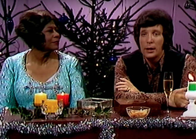 The pair are seen on the video sitting in front of a live studio audience in front of a banquet table filled with christmas accessories and surrounded by christmas trees and fairy lights.