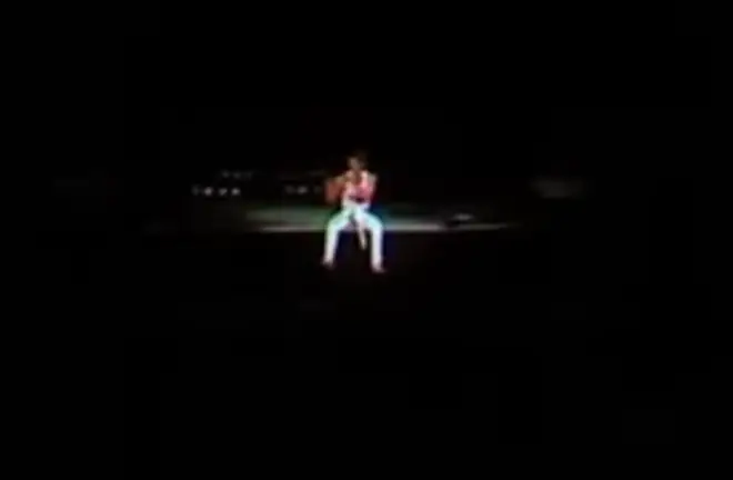 The camera then pans to an image of a tiny Freddie Mercury, feet dangling over the edge of the stage and surrounded by darkness, with only the sounds of an invisible roaring crowd singing every note back to him for company.