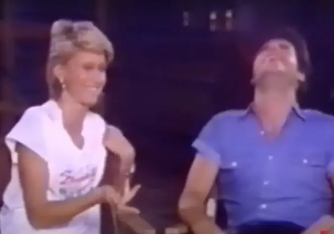 Olivia Newton-John gestures to a laughing Travolta and says to the camera, "This is a typical day..."