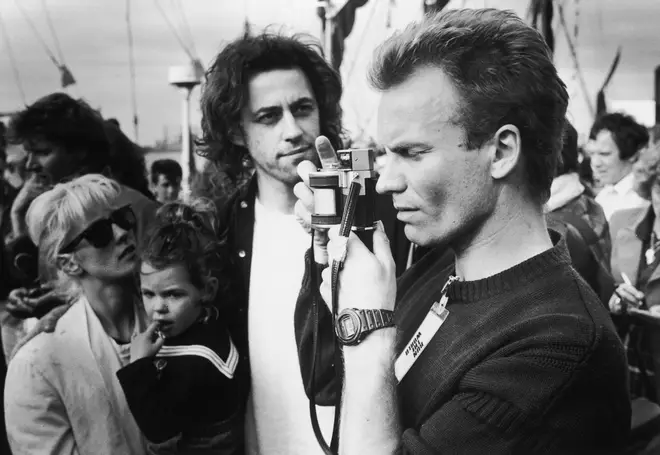 Sting takes a picture at the Sport Aid charity run, London, May 25 1986. Behind him, the event's organizer, Bob Geldof (centre) can be seen with his girlfriend Paula Yates (left)