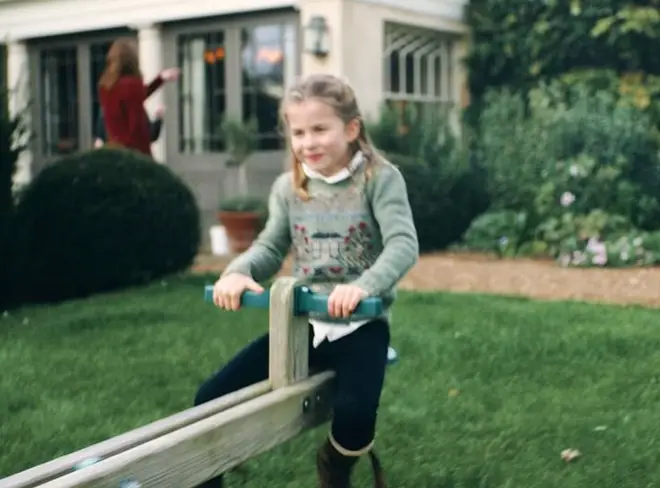 Princess Charlotte can be seen playing on a seesaw with her mother in the background in a still from the video, pictured.