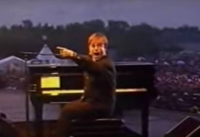 The footage opens with Elton, on stage in front of an audience of thousands, turning to look back stage and furiously gesticulating to what looks to be his stage hand.