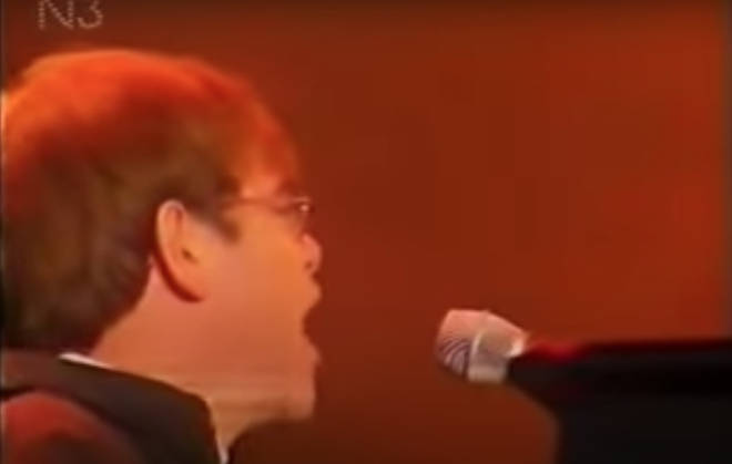 As the cameraman zooms in closer to Elton at the piano, however, his eyes betray him as he continues to look to his left, and sporadically shouts out of earshot of the microphone.