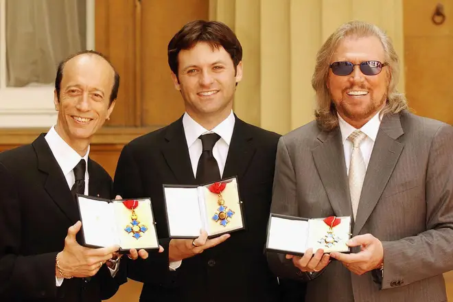 Adam Gibb receiving the CBE on behalf of his father, the late Maurice Gibb, with his uncles Barry and Robin. (Photo by ROTA/Getty Images)