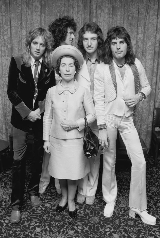Queen posing with actress and Queen Elizabeth II look-alike, Jeannette Charles, September 1974. The group are (left to right) drummer Roger Taylor, guitarist Brian May, bassist John Deacon and singer Freddie Mercury