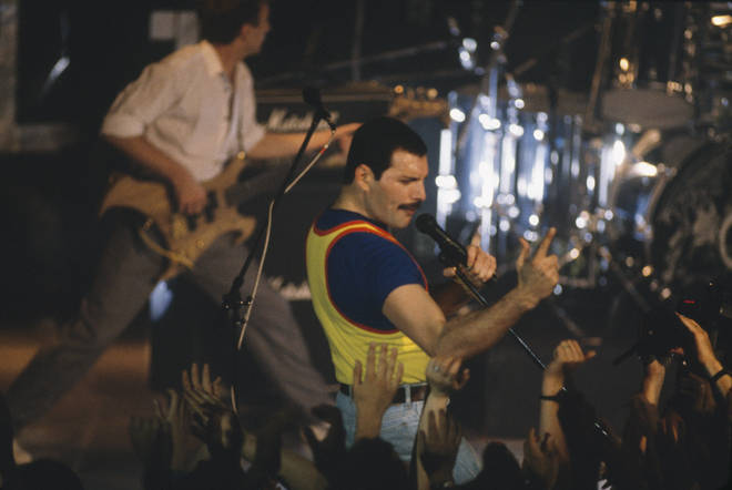 Side of stage shot of Freddie Mercury and John Deacon playing to a crowd in 1986.